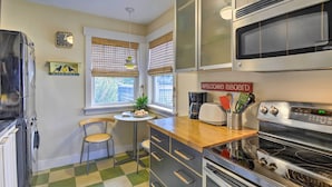 A kitchen with a checkered floor, a microwave, an oven, a coffee maker, and a small table with a chair.