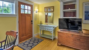 A room with a wooden door, a desk with drawers, a television on a wooden dresser, and a bookshelf with books.