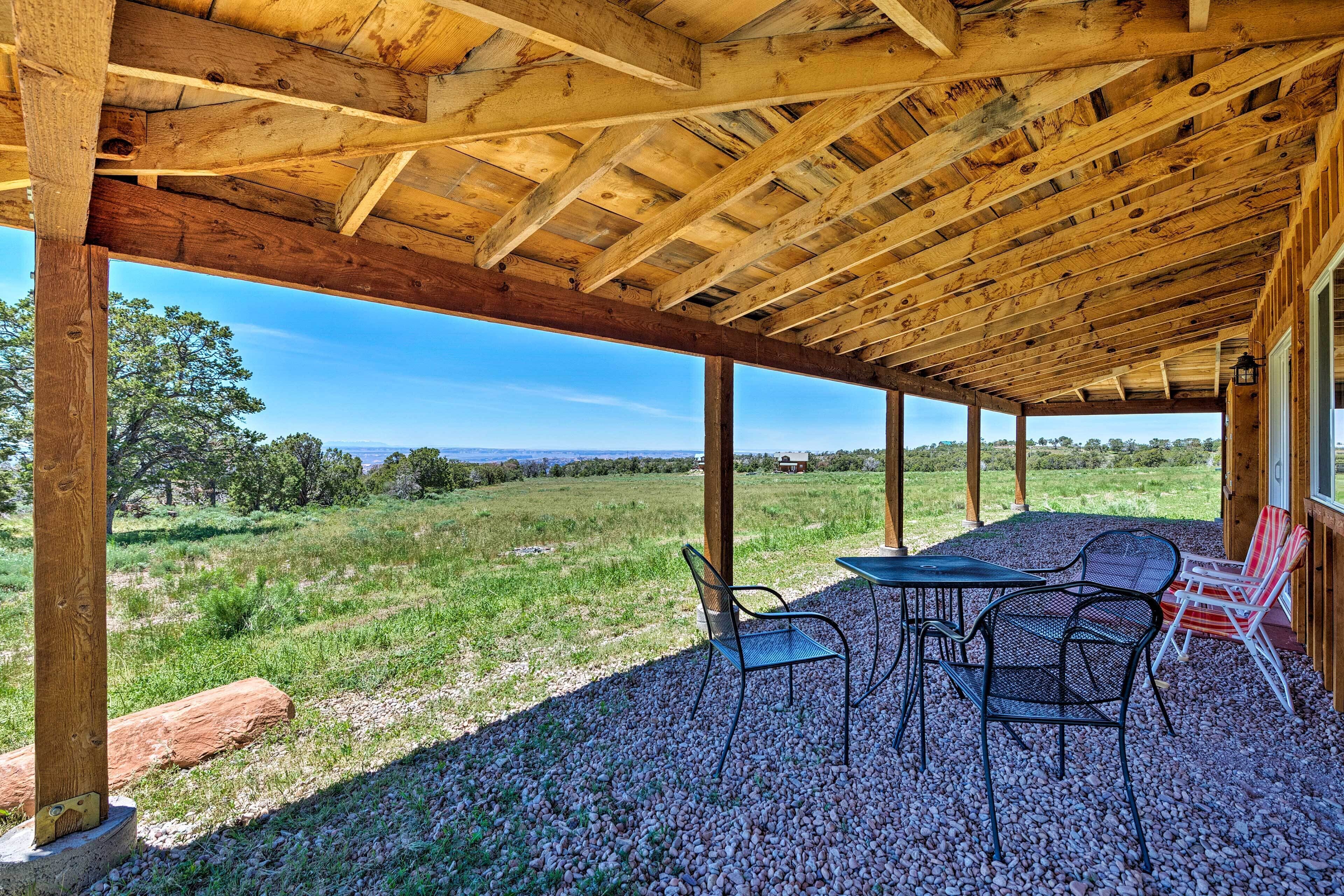 Eine überdachte Terrasse im Freien mit Holzbalken, einem Tisch, Stühlen und Blick auf eine Wiese.