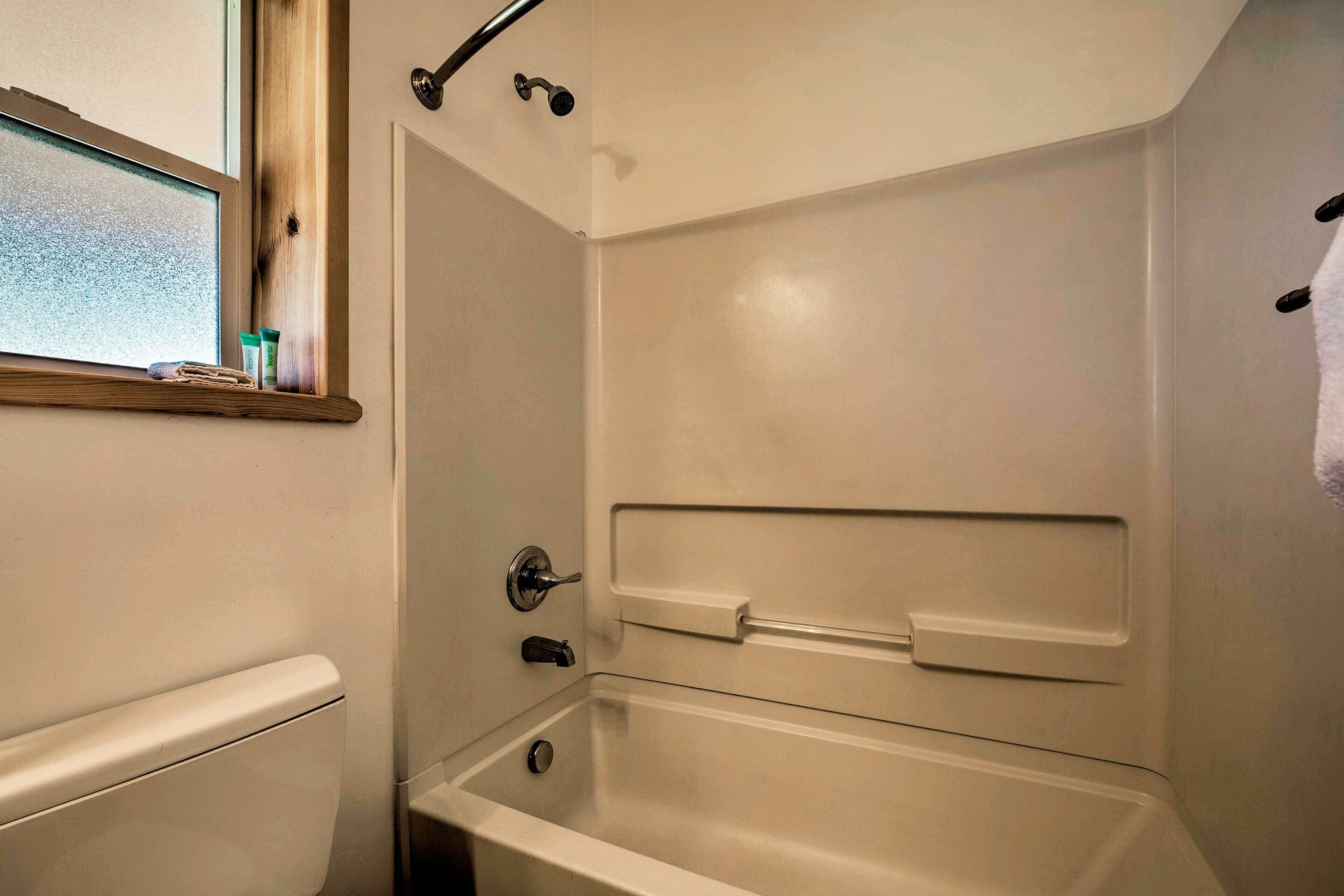 Een badkamer met een bad, een raam met uitzicht en een plank met toiletartikelen.