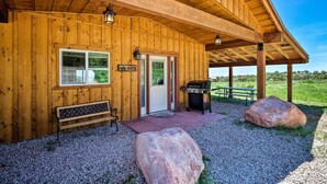 Una baita di legno con un portico coperto, un barbecue, una panchina e un cartello con scritto 'Vista'.