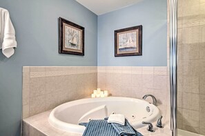 Un baño con bañera, lavamanos y ducha. Hay cuadros enmarcados en la pared y una toalla colgada.