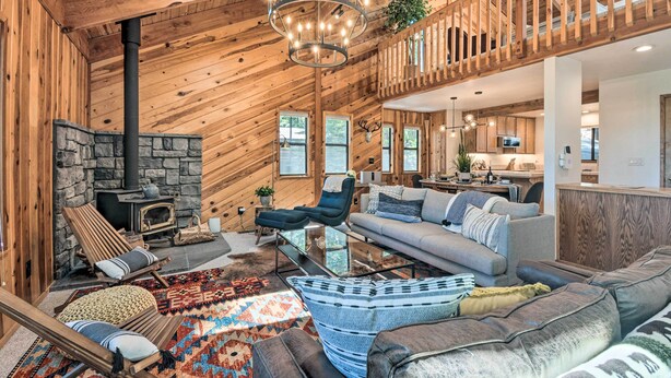 A spacious living area with a stone fireplace, wooden ceiling, and a balcony overlooking the kitchen. - Hike, Fish, & Relax: Family Arnold Cabin (Arnold)