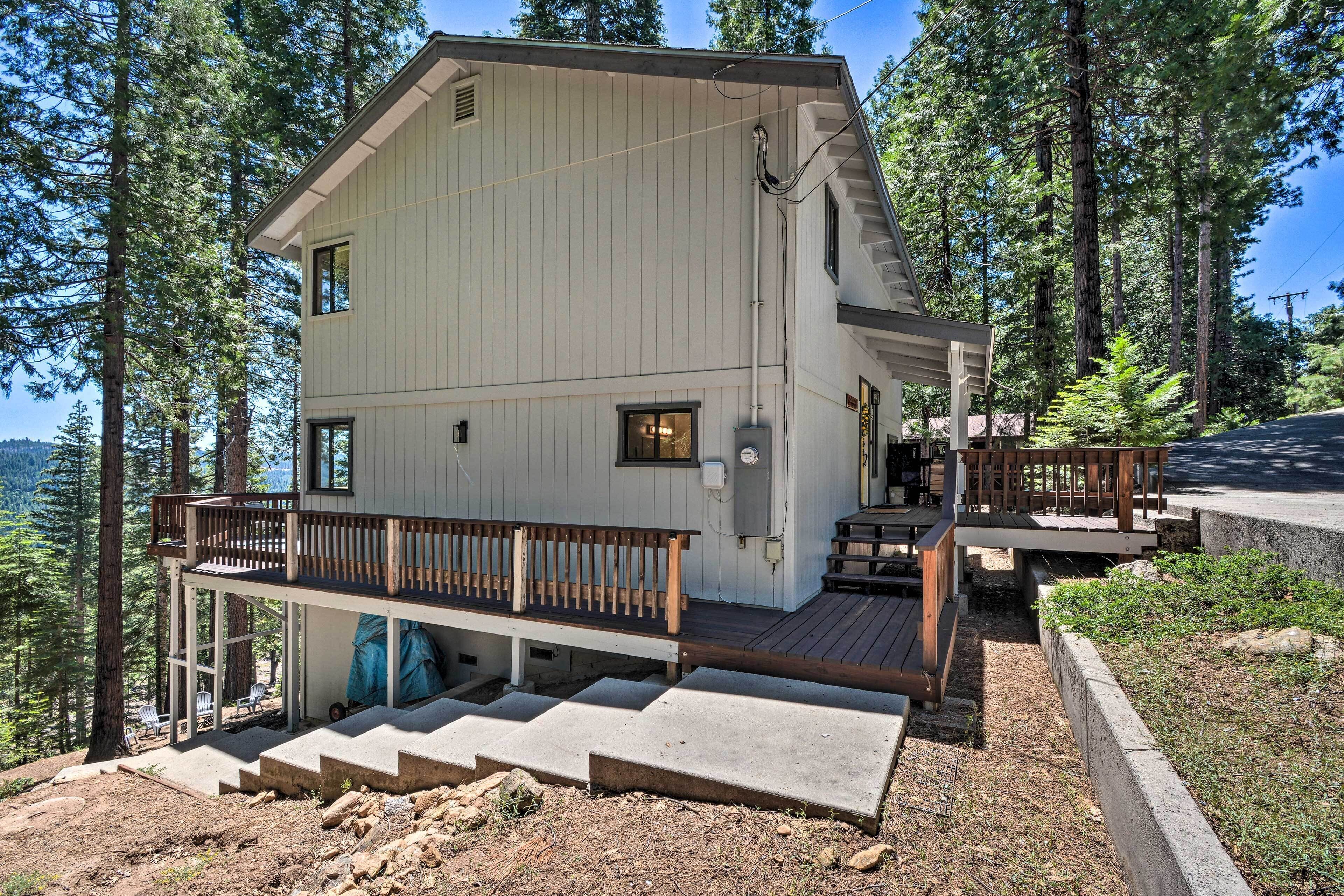 A two-story cabin with a wooden deck and a covered outdoor seating area, surrounded by tall trees.