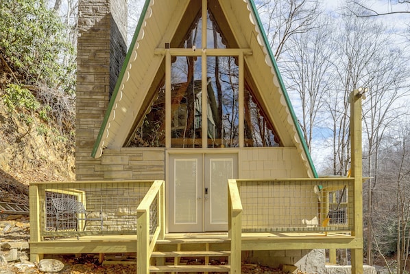 A wooden cabin with a triangular roof, a balcony with a railing, and a stone wall.