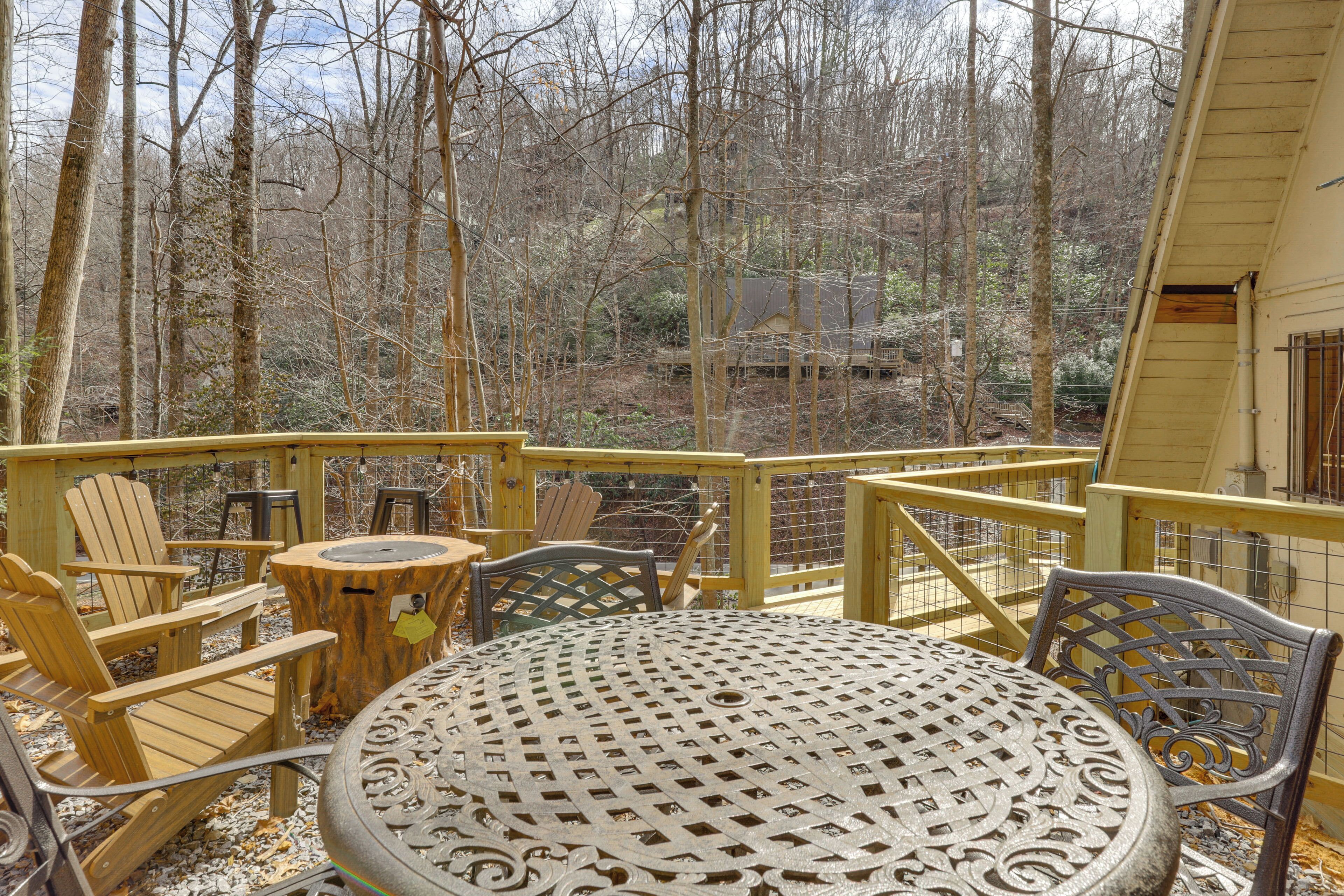 A wooden deck with Adirondack chairs, a metal table, and a view of a forested area.