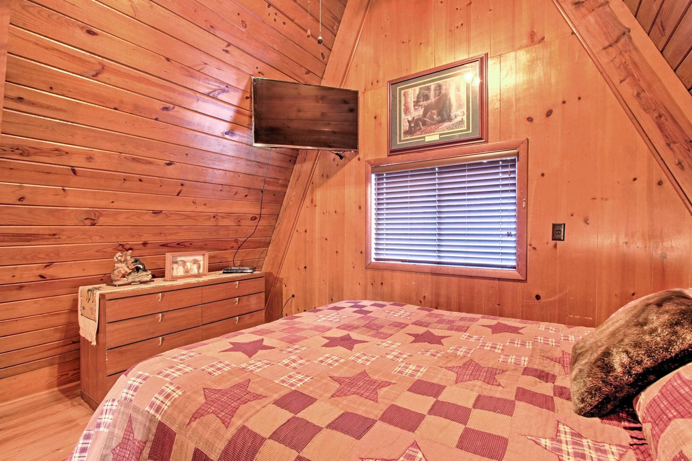 Een gezellige slaapkamer met houten wanden, een bed met quilt met stermotief, een dressoir, een flatscreen televisie en een raam met zonwering.