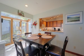 A dining area with a table set for four, a kitchen in the background, and a view of the outdoors through large windows. - All-season Base! Unit w/ Balcony in Beech Mountain (Banner Elk)