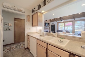 A kitchen with a double sink, wooden cabinets, a dishwasher, and a large window with a view.