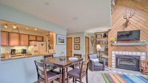Een moderne keuken met houten kastjes, een eettafel met stoelen, een open haard en een flatscreen televisie erboven bevestigd.