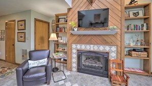 Een woonkamer met een open haard, een televisie en houten planken met boeken en decoratieve objecten.