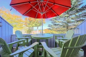 A patio with a red umbrella, green Adirondack chairs, and a small table. - All-season Base! Unit w/ Balcony in Beech Mountain (Banner Elk)