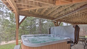 Un jacuzzi bajo una pérgola de madera con vistas a árboles y una mesa de picnic cerca.