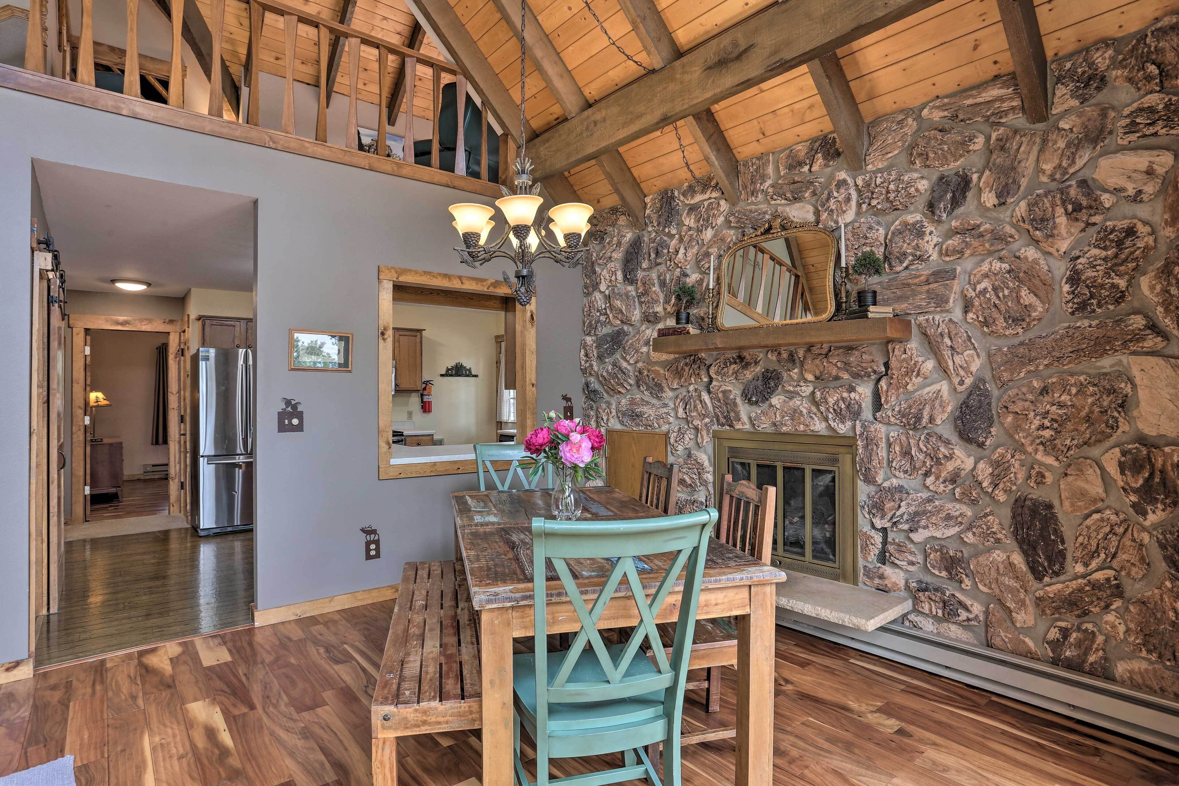 A dining area with a stone wall, wooden ceiling beams, and a chandelier.
