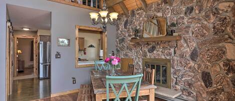A dining area with a stone wall, wooden ceiling beams, and a chandelier.