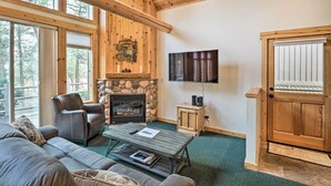 A cozy living room with a stone fireplace, leather sofa, and a television mounted on the wall.