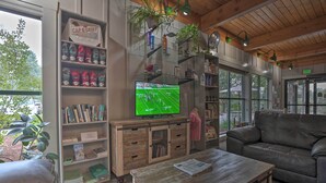 A cozy room with a television displaying a sports game, wooden furniture, and a view of the outdoors.