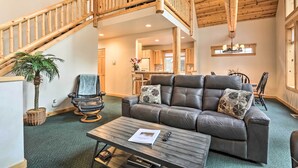 A spacious living area with a wooden staircase, leather sofa, and a dining area in the background.