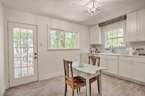 A kitchen with white cabinets, a dining table with chairs, and two windows providing natural light. - 'blackberry Roost' Home ~ 4 Mi to Downtown Salado (Salado)