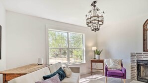 A living room with a wooden table, a white sofa with cushions, a purple armchair, a chandelier, and a fireplace. - 'blackberry Roost' Home ~ 4 Mi to Downtown Salado (Salado)