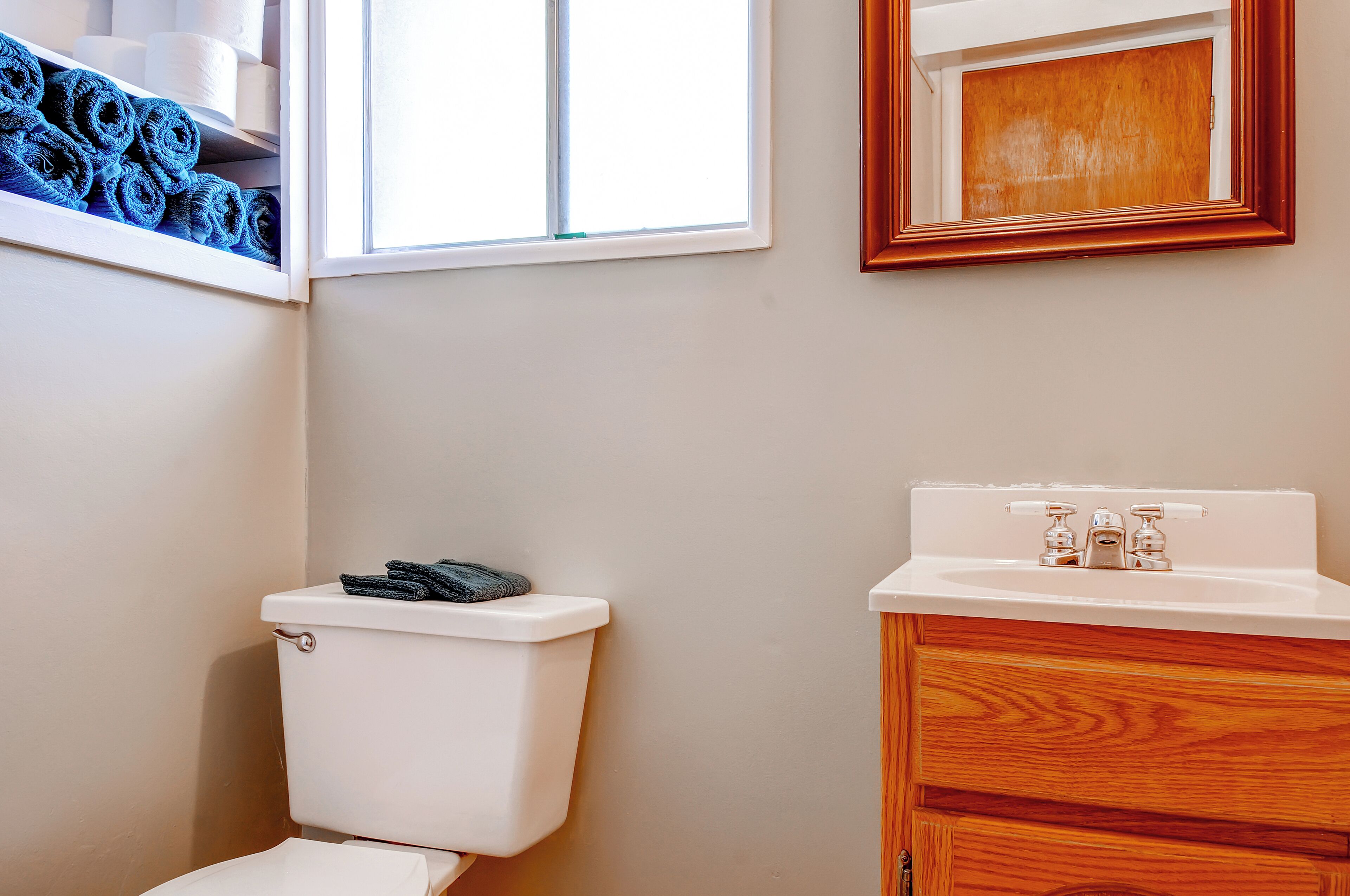 A bathroom with a toilet, a sink, and a window with rolled towels.