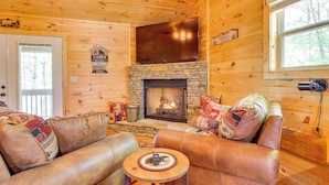 A cabin interior with a stone fireplace, leather sofas, a flat-screen TV, and a stone accent wall.