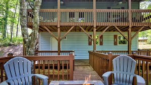A cabin with a deck, two Adirondack chairs, and a fire pit.