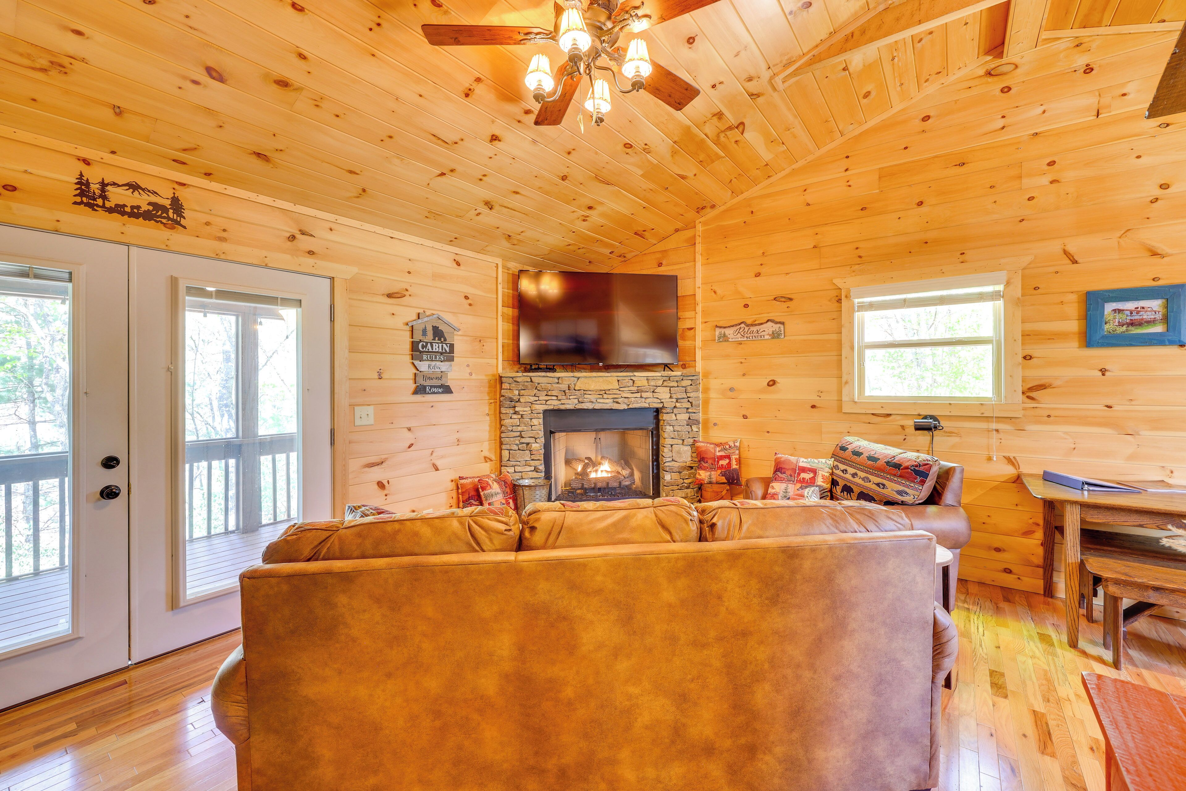 A cozy cabin interior with a stone fireplace, wooden walls, a leather sofa, and a dining area.