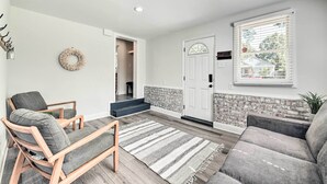 A living room with a grey sofa, a wooden chair, a striped rug, and a brick-patterned wall. - Chic Charlotte Retreat < 3 Miles to Downtown! (Charlotte)