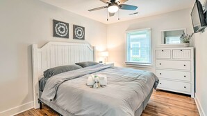 A bedroom with a bed, a ceiling fan, a nightstand with a lamp, a dresser, and a window with blinds. - Chic Charlotte Retreat < 3 Miles to Downtown! (Charlotte)