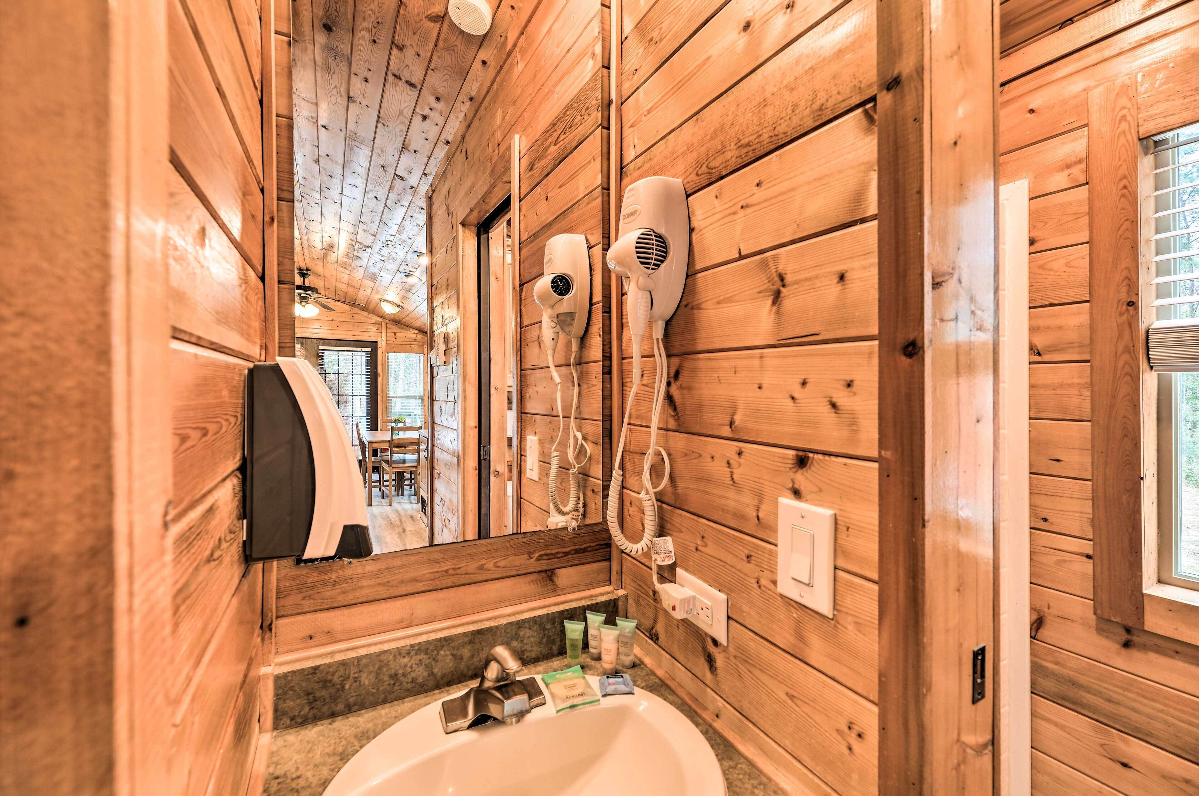 A wooden cabin-style bathroom with a sink, hair dryers, and a mirror.