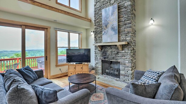 A spacious living room with a stone fireplace, a large flat-screen TV, and a balcony with a scenic view. - Getaway Chalet in Mars Hill w/ Hot Tub & Views! (Mars Hill)
