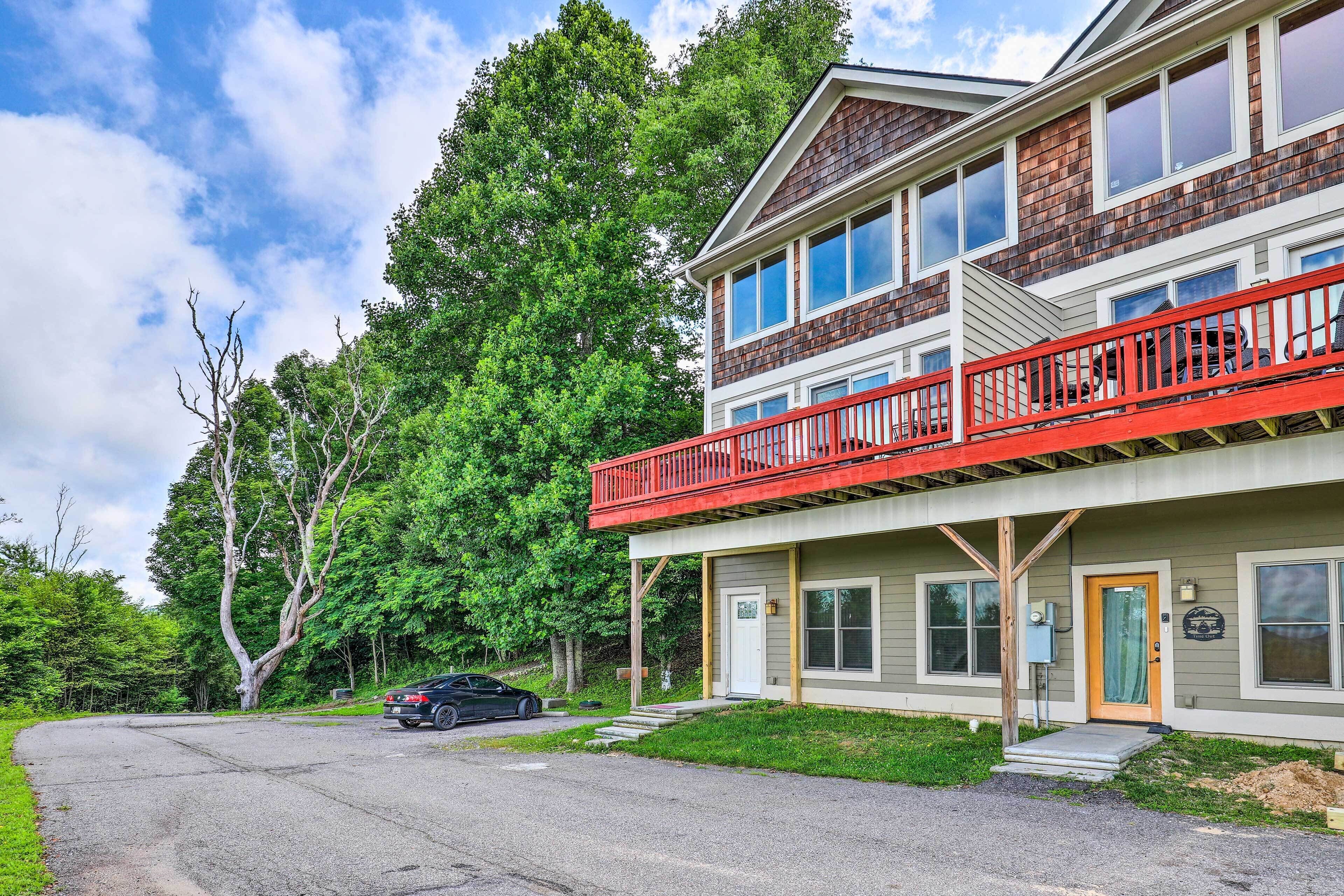 A two-story building with a red balcony, a front door, and a parked car.