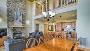 A spacious living room with a stone fireplace, a dining area with wooden furniture, and a kitchen with wooden cabinets. - Getaway Chalet in Mars Hill w/ Hot Tub & Views! (Mars Hill)