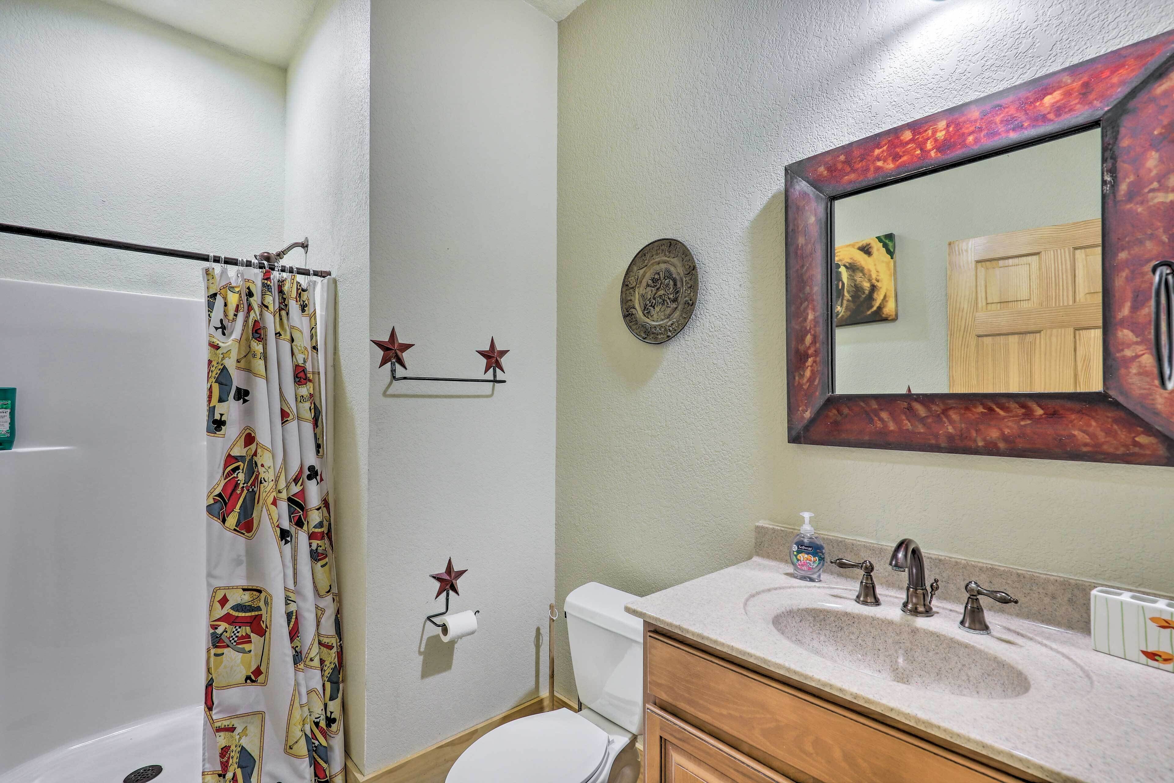 Un baño con cortina de ducha temática de juego de cartas, un inodoro, un lavabo con dispensador de jabón y un espejo con marco decorativo.