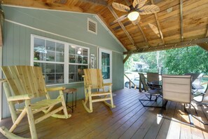A wooden deck with rocking chairs and a table, a covered area with a ceiling fan, and a view of the outside.