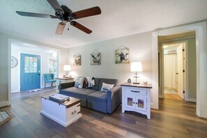 A living room with a ceiling fan, a blue door, a grey sofa, a white side table, and a lamp.