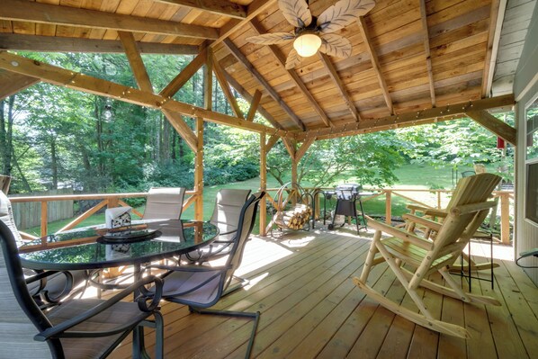 A wooden deck with a glass table and chairs, surrounded by a wooden fence, and a rocking chair.