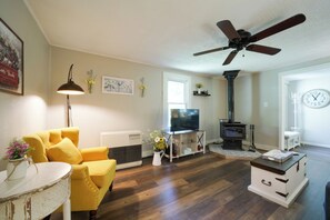 A living room with a yellow sofa, a white coffee table, a ceiling fan, a fireplace, and a TV.