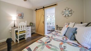 A bedroom with a bed, a desk, a chair, a sliding door, and a wall decoration. - Charming Waynesville Cottage < 2 Mi to Main St (Waynesville)