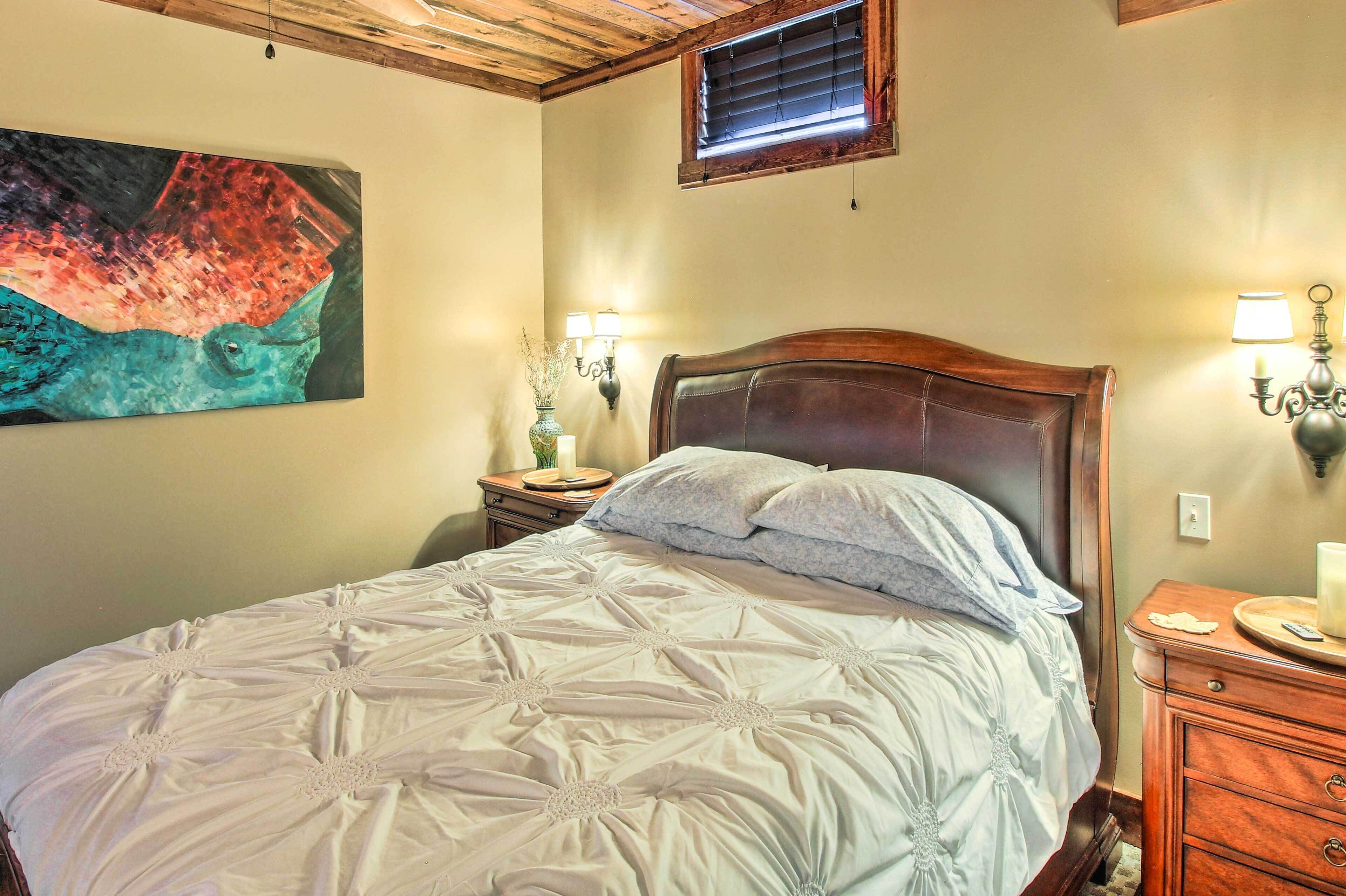 A bedroom with a large bed, two bedside tables with lamps, a wall-mounted artwork, and a window with blinds.
