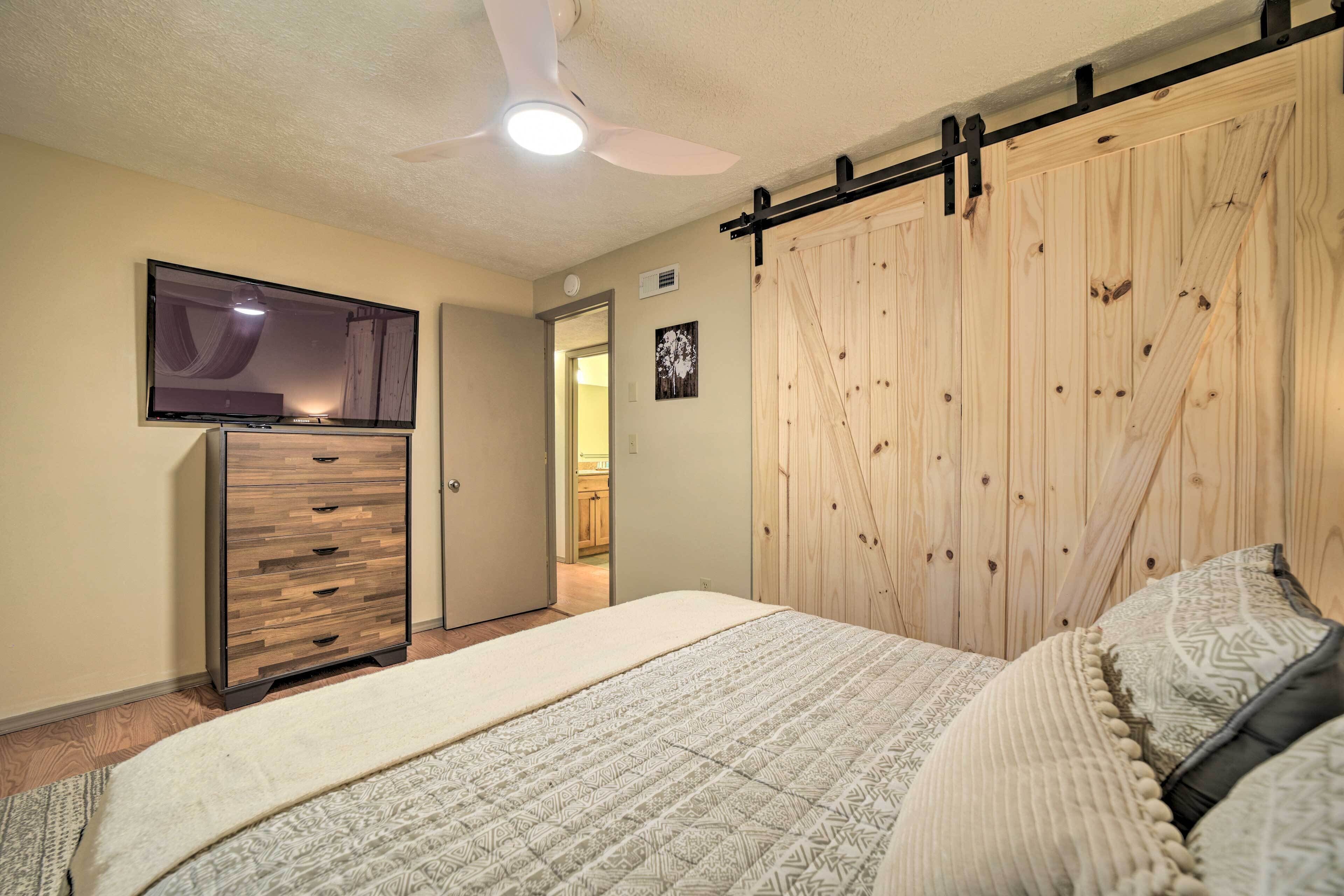 A bedroom with a bed, a dresser, a TV mounted on the wall, and a wooden wardrobe.
