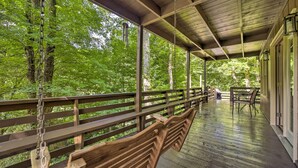 A wooden deck with a railing, a table, and chairs, overlooking a forested area.