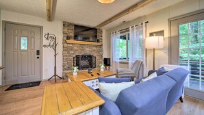 A cozy living room with a stone fireplace, a blue sofa, a wooden coffee table, and a lamp.