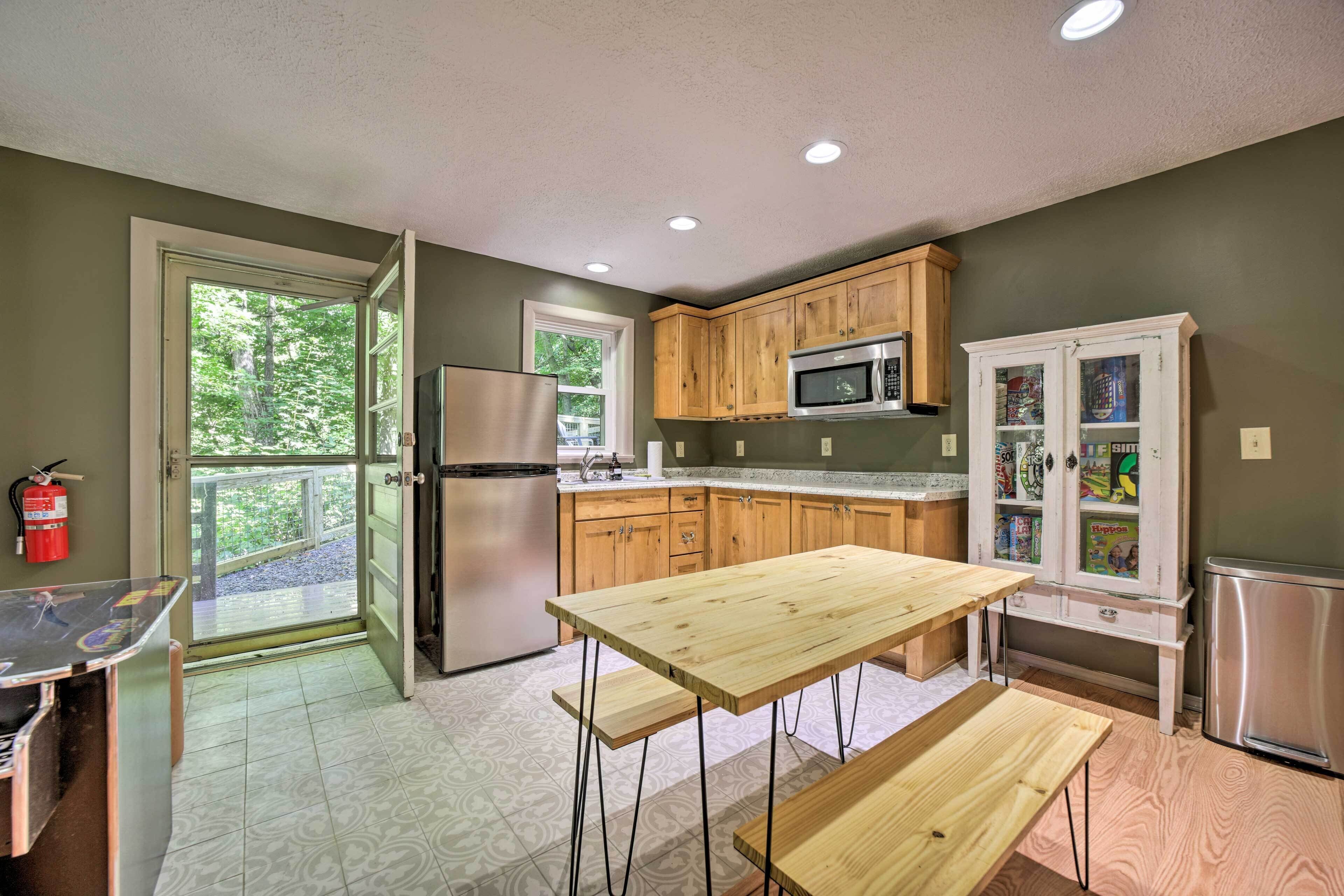 A kitchen with wooden cabinets, a stainless steel refrigerator, a microwave, and a glass-fronted cabinet with children's books.