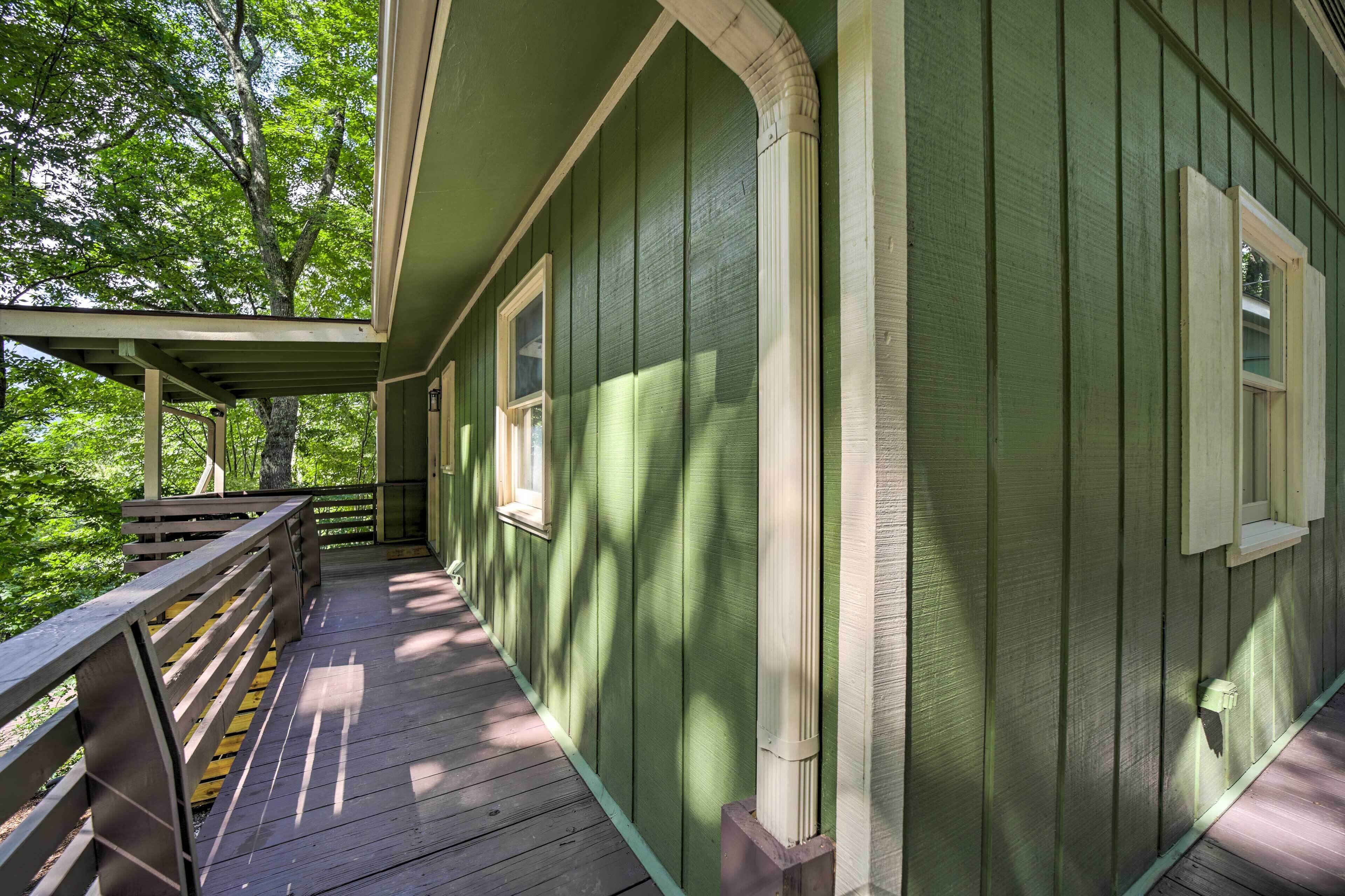 A wooden deck with a railing, a covered porch, and a green building with windows.