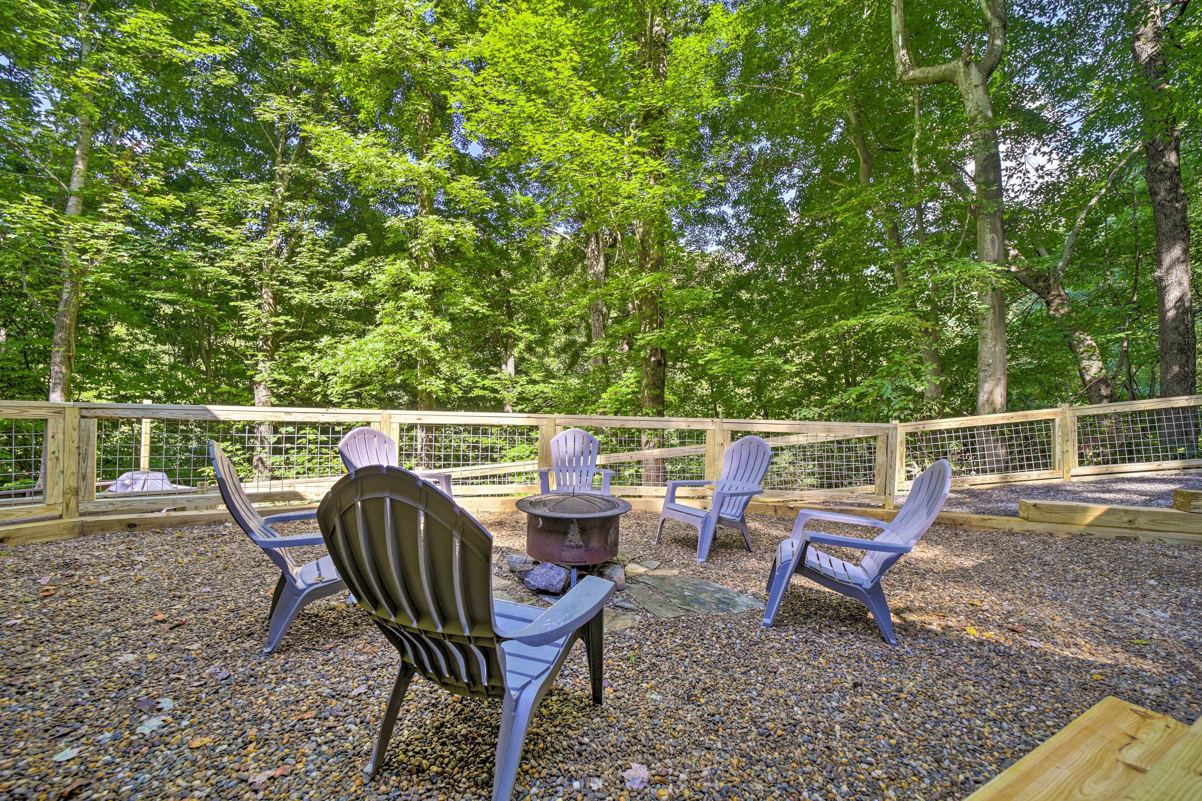 Een buitenruimte met Adirondack-stoelen en een vuurkuil, omgeven door een houten hek en grind, gelegen in een bebost gebied.