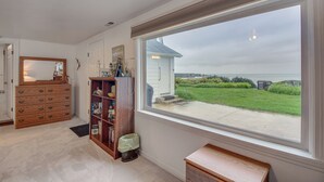 Una habitación con un ventanal grande, un aparador de madera, una estantería y un pequeño banco.