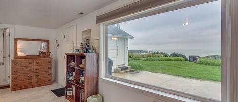 A room with a large window, a wooden dresser, a bookshelf, and a small bench.