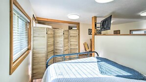 Une chambre à coucher avec un lit, un téléviseur fixé au mur et une fenêtre avec des stores.